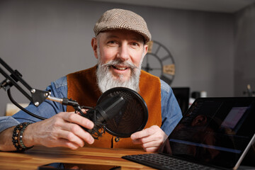 Studio podcast avec un micro et un ordinateur tablette et un homme souriant au look stylé et vintage avec une barbe hipster - 769783352