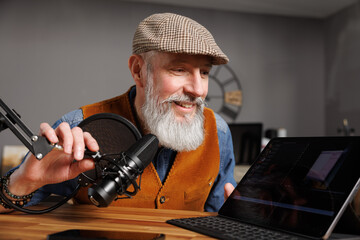 Studio podcast avec un micro et un ordinateur tablette et un homme souriant au look stylé et vintage avec une barbe hipster - 769783565