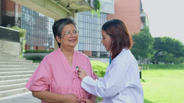 Asian careful caregiver or doctor taking care of the elderly Asian patient in hospital park. Concept of happy retirement with care from caregiver and Savings and senior health insurance. elderly care
