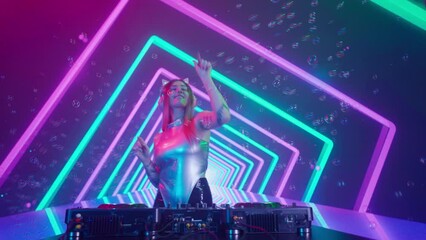 Attractive female on digital wall colorful visual graphic background. Young woman dj dancing, plays music on turntables mixer at night club, looks at camera.