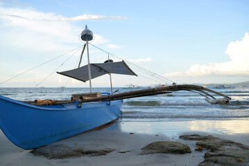 A traditional Filipino fishing boat Bangca standing in the evening on the seashore sand beach in Sabang, Puerto Princesa, Palawan island. Sunset sky is at the background