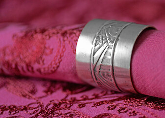Antique silver napkin ring with red and pink embroided napkin and tablecloth. Selective focus