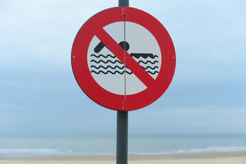 Round red prohibition sign by the coastline indicating swimming is not allowed in this area. Selective focus