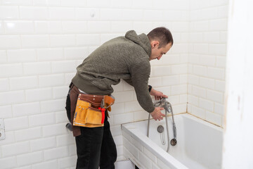 A male plumber with wrench repairs the faucet in the bathroom. replacement and maintenance of plumbing. handyman service. small business.