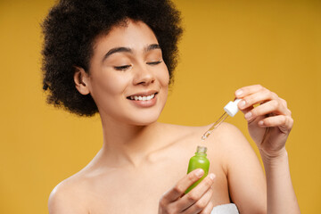 Obraz na płótnie Canvas Beautiful young Latin woman holding green bottle applying serum to face, skin care, moisturizing