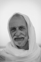 An elderly man with a gray beard and headscarf, wearing traditional oriental clothes. He looks directly at the camera with a wrinkled face exuding a sense of maturity and wisdom. Black and white image