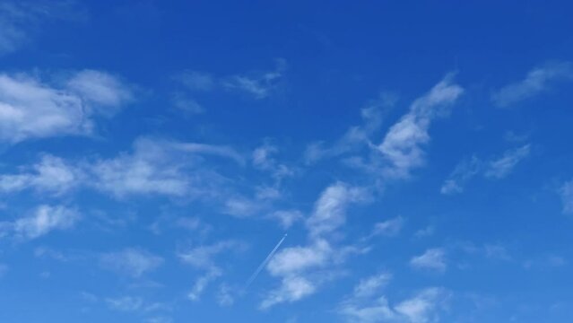 An airplane with jet contrail flying over the clouds in the blue sky. Cloudscape with blue sky background.