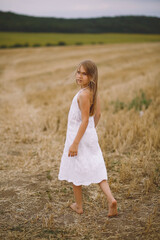 Charming blonde girl in summer dress posing on the field at summertime. Summer photoshooting. Summer season. Beautiful girl