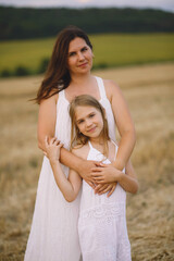 Happy mother in summer dress hugs her daughter on the field.  Photoshooting mother and daughter. Summer season. Family concept