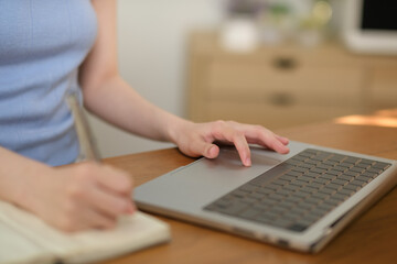 A woman is typing on a laptop while writing in a notebook