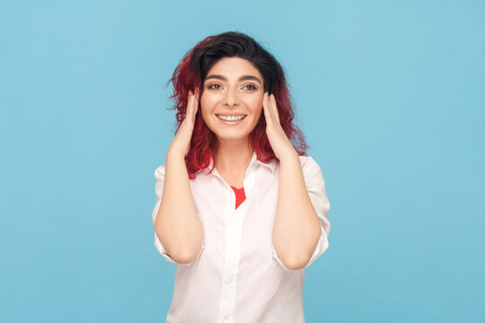 Portrait of smiling positive optimistic woman with fancy red hair dreaming about pleasant future, enjoying moment, wearing white shirt. Indoor studio shot isolated on blue background.