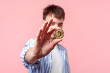 Portrait of attractive brunette young man wearing shirt holding out golden bitcoin cryptocurrency...