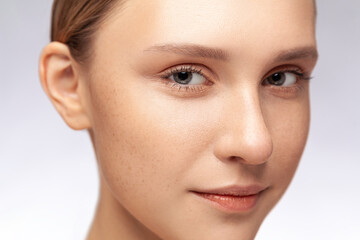 Obraz premium Closeup portrait of beautiful winsome with perfect skin and natural makeup looking at camera with calm charming smile. Indoor studio shot isolated over gray background.