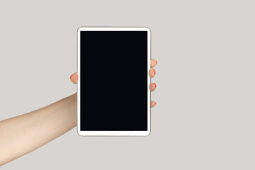 Closeup of woman hand showing digital tablet with black blank screen copy space for advertisement. Indoor studio shot isolated on gray background.