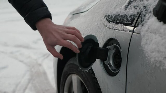Male hands insert power connector into EV, snow closeup. Unrecognizable person connects charging cable to an electric car. Charging batteries an electric vehicle or PHEV in winter