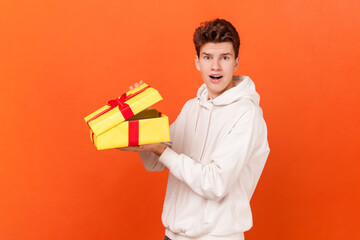 Portrait of shocked scared young man wearing white hoodie opening yellow present box, being...