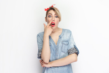 Portrait of funny crazy blonde woman wearing blue denim shirt and red headband standing keeps...