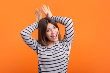 Portrait of funny playful positive woman with brown hair raised her arms showing rabbit ears,...