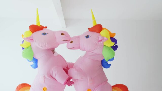 Two People Dancing Joyfully in Unicorn Costumes With Rainbow Manes Indoors
