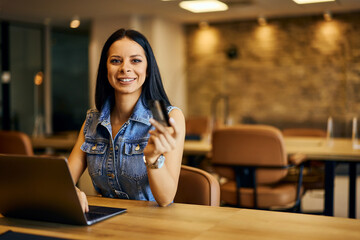 Portrait of a smiling businesswoman, posing for the camera while working online and holding a credit card. - 769831527