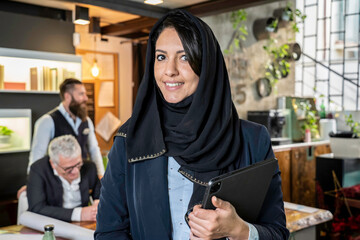 Confident businesswoman in hijab with digital tablet at a modern coworking office. Embodying leadership and cross-cultural empowerment in a professional setting. A portrait of diversity in harmony.