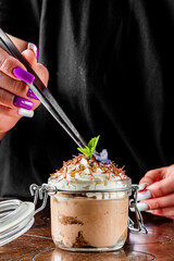 A person delicately garnishes a creamy dessert with a sprig of mint, adding the final touch to food presentation