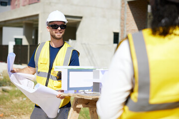 worker or architect holding blueprint paper and talking with coworker at construction site