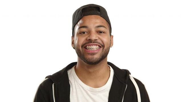 Bright-eyed young adult expressing joy with a visible braces smile, wearing casual modern clothes on a white background, symbolizing positivity and dental health. Camera 8K RAW. 