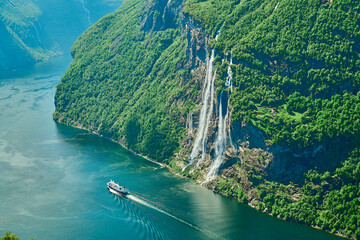 Seven Sisters waterfall in the beautiful Geiranger Fjord, a well known travel destination for cruise ships, offers spectacular views to the norwegian landscape with snow covered mountain ranges. - obrazy, fototapety, plakaty