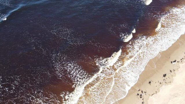 Waves breaking onto a beach in Scotland filmed from directly above. The water is brown from peat in a nearby river.