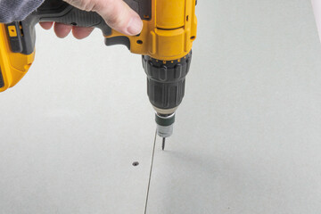 a contractor's hand holding an electric drill with a drywall screw clutch setter ready to drive...