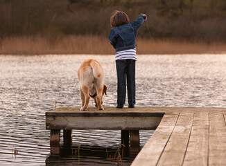 Child playing near water with her dog.
