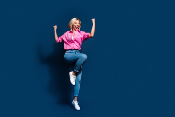 Fototapeta na wymiar Full length photo of lovely young lady raise fists jump lottery winner dressed stylish pink garment isolated on dark blue color background