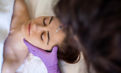Top view of a woman recieving injection of anti-aging botox filler to forehead from professional...