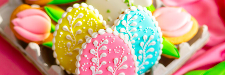 background banner greeting card for Happy Easter with set colorful eggs, Easter cake and flowers tulips gingerbread cookies in egg box on pink silk fabric background, flat lay food banner