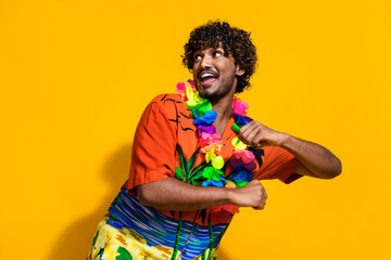 Portrait of overjoyed guy with afro hair wear hawaii flower necklace dancing look at promo empty space isolated on yellow color background