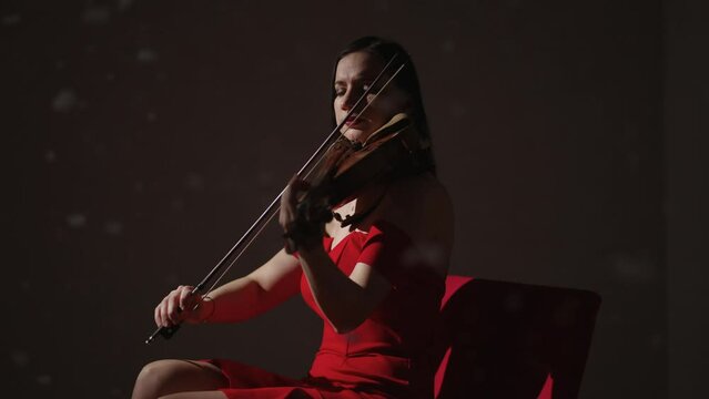 Emotional Woman Violinist In Red Dress Playing Romantic Melody In Studio, Snowflakes Flying Up