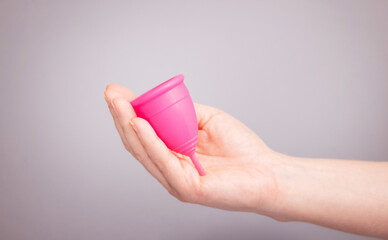 A woman holds a menstrual cup in her hands. pink menstrual cup on a gray background. close-up of a...