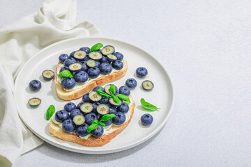 Fototapeta na wymiar Fresh bread sandwiches with sweet blueberries, cream cheese and basil leaves. Good morning concept