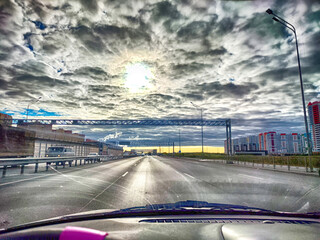 View of the highway from driver's seat from the car salon and road with dramatic clouds and sun....