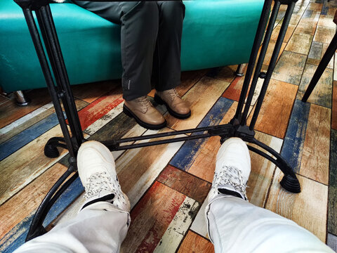 Legs of two seated people facing each other, focus on footwear. Two People Sitting Opposite Each Other in a cafe or restaurant Room With a Colorful Floor