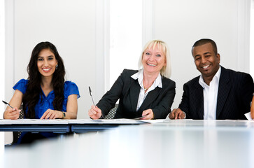 Office colleagues with bright smiles for the camera working together on a project in a neutral office environment.