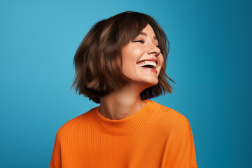 Portrait of a beautiful woman looking up and smiling, wearing an orange sweater against a blue background
