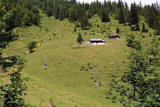 Suspension cable car on the background of a mountain slope covered with green grass and wooden hotel buildings