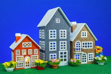Three unusual beautiful toy houses on a green surface and a blue background
