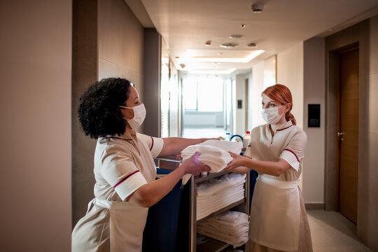 Housekeeping staff exchanging fresh towels in hotel hallway while wearing face masks