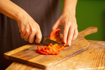 Italian bread and ingredients - parmesan, olive oil, tomato, spice and herbs. Portrait of chef's hands cuts red pepper slices on a pizza. Horizontal image.
