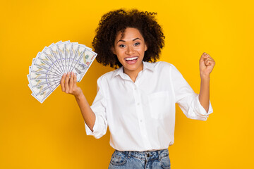 Photo of attractive lady raise fist success achieve hundred banknotes isolated on yellow color...