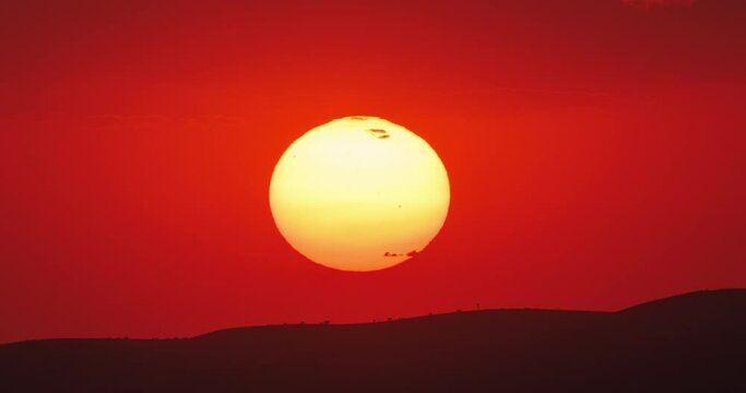 Epic dramatic view of sun appears from behind the clouds and sinks below the horizon. Timelapse of red sunset in desert. Concept of end of the day, big hot circle down. Night will come soon