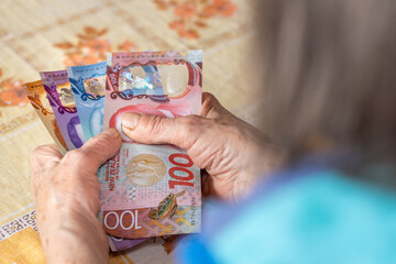 Household budget of older people in New Zealand. Economic concept, Pensioner woman holds several 50, 10 and 100 dollar banknotes in her hands, Financial situation of elderly people